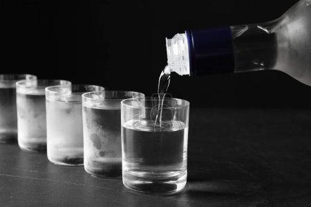 Pouring vodka from bottle in glass on grey table, closeup