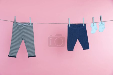Photo for Different baby clothes drying on laundry line against pink background - Royalty Free Image