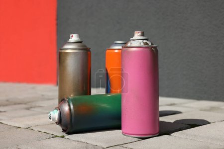 Photo for Cans of different spray paints on pavement near wall, closeup - Royalty Free Image