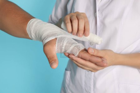 Photo for Doctor applying bandage onto patient's hand on light blue background, closeup - Royalty Free Image