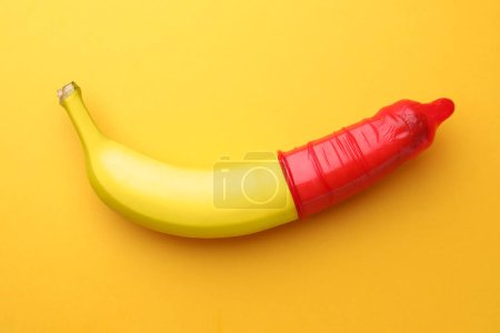 Téléchargez les photos : Banane avec préservatif sur fond orange, vue de dessus. Concept de sexe sûr - en image libre de droit