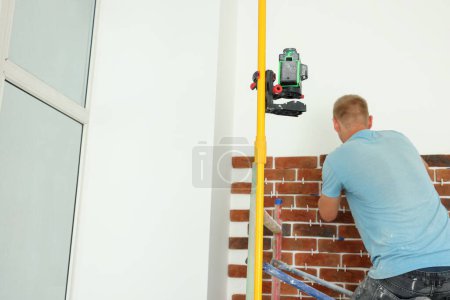 Professioneller Baumeister mit Kreuzlinien-Laserwaage beim Kleben von Ziersteinen an der Wand, Rückseite. Verlegung von Fliesen