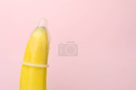 Téléchargez les photos : Banane avec préservatif sur fond rose, gros plan et espace pour le texte. Concept de sexe sûr - en image libre de droit