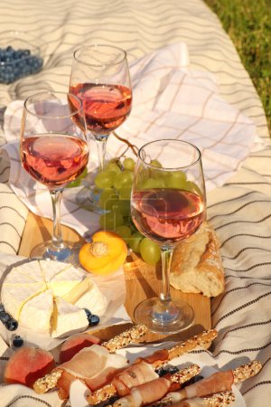 Gläser mit köstlichem Rosenwein und Essen auf weißer Picknickdecke im Freien