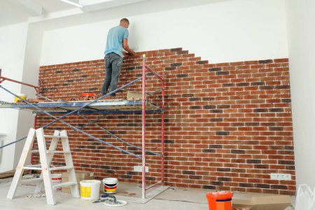 Photo for Professional builder gluing decorative bricks on wall in room. Tiles installation process - Royalty Free Image