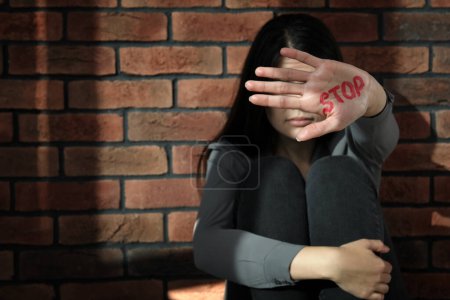 Foto de Concepto de violencia doméstica. Mujer escondiendo su cara, concéntrate en la mano con la palabra escrita Stop - Imagen libre de derechos