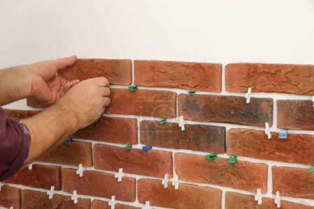 Professional builder installing new brown decorative bricks on wall, closeup