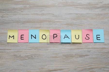 Foto de Notas coloridas del papel con la palabra Menopausia en la mesa de madera, puesta plana - Imagen libre de derechos