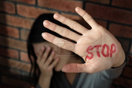 Foto de Concepto de violencia doméstica. Mujer infeliz cerca de la pared de ladrillo, se centran en la mano con la palabra escrita Stop - Imagen libre de derechos