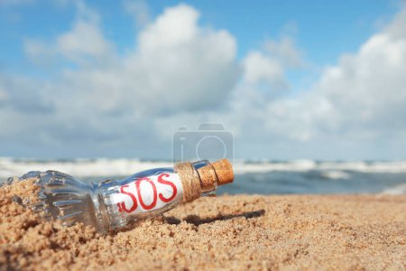 Botella de vidrio con mensaje SOS en arena cerca del mar, espacio para texto