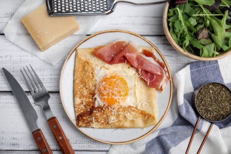 Delicious crepe with egg served on white wooden table, flat lay. Breton galette