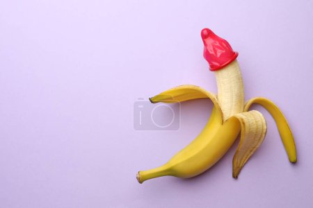 Téléchargez les photos : Banane avec préservatif sur fond lilas, vue de dessus et espace pour le texte. Concept de sexe sûr - en image libre de droit