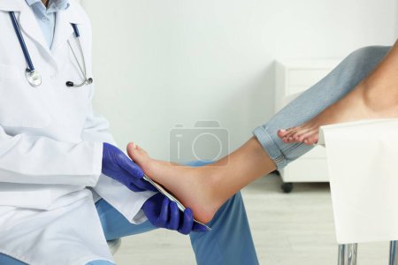 Männlicher Orthopäde passt Einlegesohle am Fuß des Patienten im Krankenhaus an, Nahaufnahme