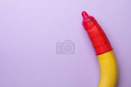 Téléchargez les photos : Banane avec préservatif sur fond lilas, vue de dessus et espace pour le texte. Concept de sexe sûr - en image libre de droit