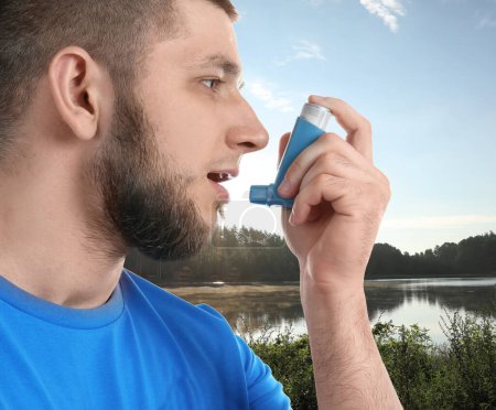Photo for Man using asthma inhaler near lake. Emergency first aid during outdoor recreation - Royalty Free Image