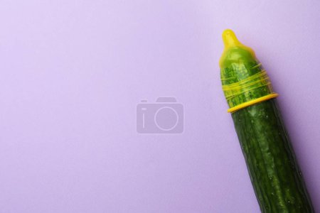 Téléchargez les photos : Concombre avec préservatif sur fond lilas, vue de dessus et espace pour le texte. Concept de sexe sûr - en image libre de droit