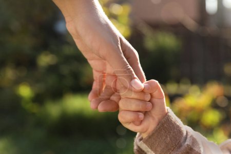Daughter holding mother's hand outdoors, closeup view
