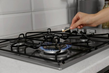 Woman lighting gas stove with match in kitchen, closeup