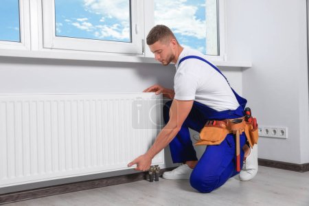 Téléchargez les photos : Professional plumber installing new heating radiator in room - en image libre de droit