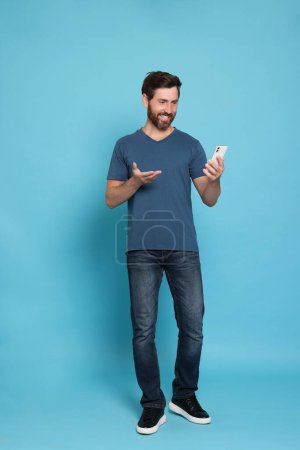 Handsome man having video chat on phone against light blue background