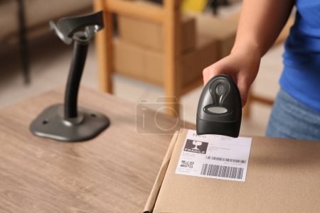 Téléchargez les photos : Employé de bureau de poste avec scanner lisant le code à barres du colis au comptoir, gros plan - en image libre de droit