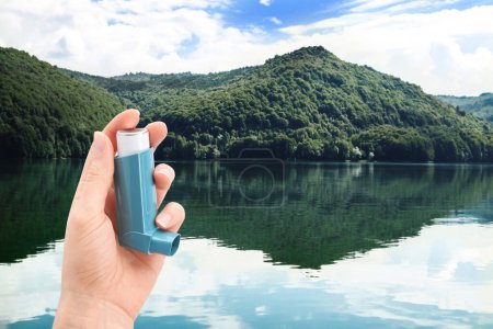 Photo for Woman with asthma inhaler near lake, closeup. Emergency first aid during outdoor recreation - Royalty Free Image