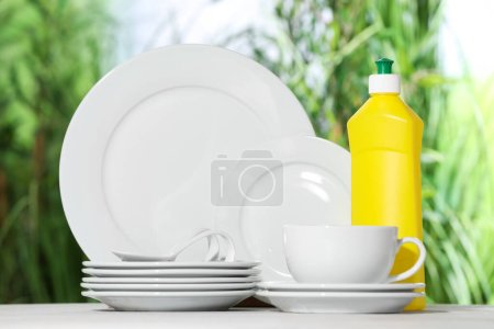 Sauberes Geschirr und Spülmittel auf weißem Tisch vor verschwommenem Hintergrund