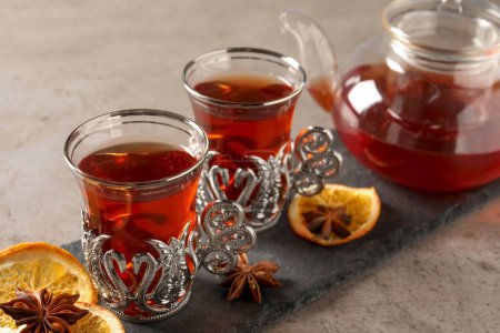 Téléchargez les photos : Assiette en ardoise avec verres de thé turc traditionnel dans des supports vintage, orange séchée et anis sur table gris clair, gros plan - en image libre de droit