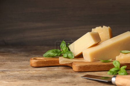 Foto de Delicioso queso parmesano con albahaca y cuchillo sobre mesa de madera. Espacio para texto - Imagen libre de derechos