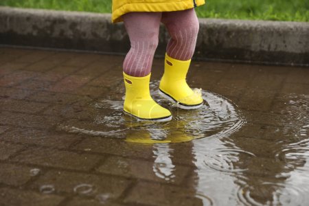 Chica caminando en charco al aire libre en tiempo lluvioso, primer plano