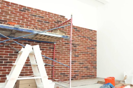 Photo for Scaffolding near wall with decorative bricks and tile leveling system in room - Royalty Free Image