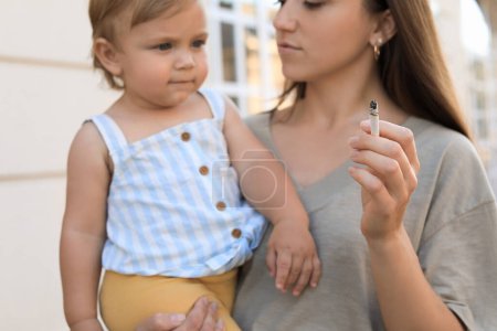 Téléchargez les photos : Mère avec cigarette et enfant à l'extérieur, concentrez-vous sur la main. Ne fumez pas près des enfants - en image libre de droit