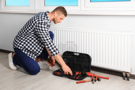 Téléchargez les photos : Plombier professionnel avec différents outils installant un nouveau radiateur de chauffage dans la pièce - en image libre de droit
