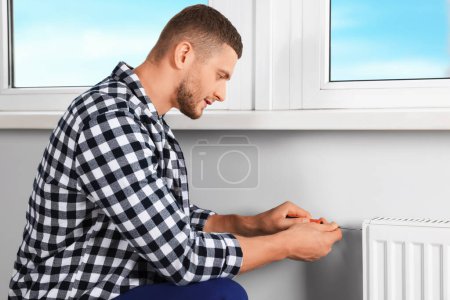 Photo for Professional plumber using screwdriver while preparing heating radiator for winter season indoors - Royalty Free Image