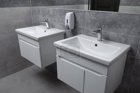 Téléchargez les photos : Intérieur des toilettes publiques avec lavabos blancs élégants et carreaux gris - en image libre de droit