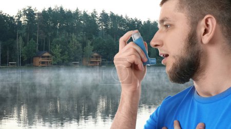 Photo for Man using asthma inhaler near lake. Emergency first aid during outdoor recreation - Royalty Free Image
