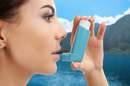 Photo for Woman using asthma inhaler near lake. Emergency first aid during outdoor recreation - Royalty Free Image
