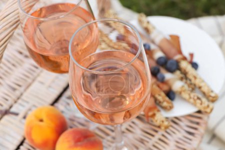 Photo for Glasses of delicious rose wine and food on picnic basket outdoors - Royalty Free Image