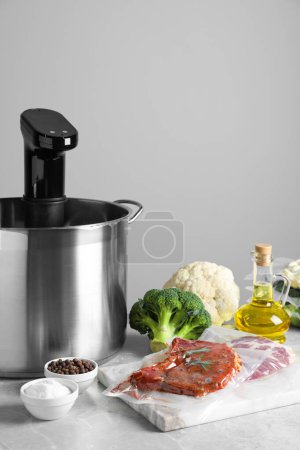 Photo for Thermal immersion circulator in pot and ingredients on light grey table. Vacuum packing for sous vide cooking - Royalty Free Image
