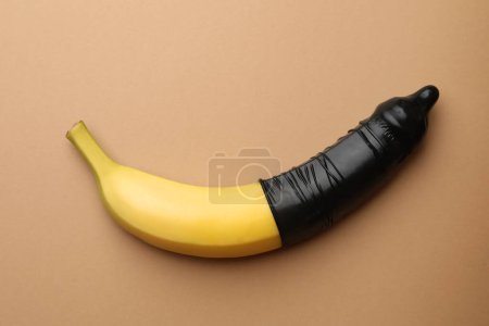 Téléchargez les photos : Banane avec préservatif sur fond orange pâle, vue de dessus. Concept de sexe sûr - en image libre de droit