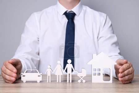 Photo for Man protecting figures of family, car and house at wooden table. closeup. Insurance concept - Royalty Free Image