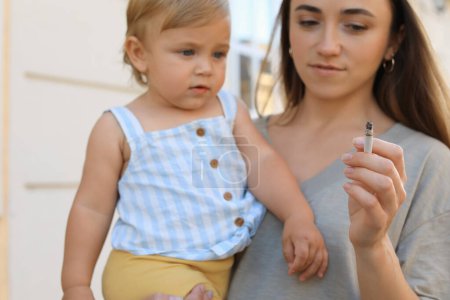 Téléchargez les photos : Mère avec cigarette et enfant à l'extérieur, concentrez-vous sur la main. Ne fumez pas près des enfants - en image libre de droit