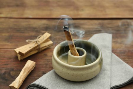 Photo for Palo Santo stick smoldering in holder on wooden table - Royalty Free Image