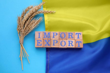 Téléchargez les photos : Mots Importation et exportation de cubes en bois, épis de blé et drapeau ukrainien sur fond bleu clair, pose plate - en image libre de droit