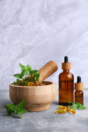 Photo for Wooden mortar with fresh green herbs, extracts and capsules on light grey table - Royalty Free Image