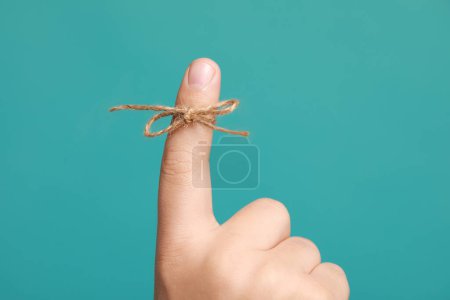 Photo for Man showing index finger with tied bow as reminder on turquoise background, closeup - Royalty Free Image