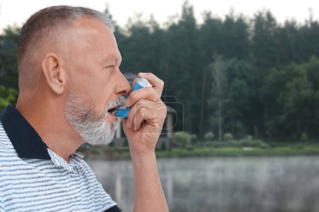Photo for Mature man using asthma inhaler near forest. Emergency first aid during outdoor recreation - Royalty Free Image