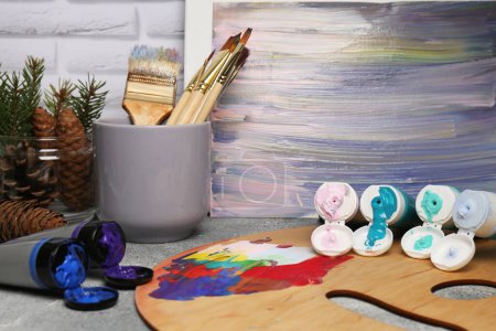 Foto de Paleta de artista, tubos de pintura colorida, pinceles y lienzo con pintura abstracta sobre tabla texturizada - Imagen libre de derechos