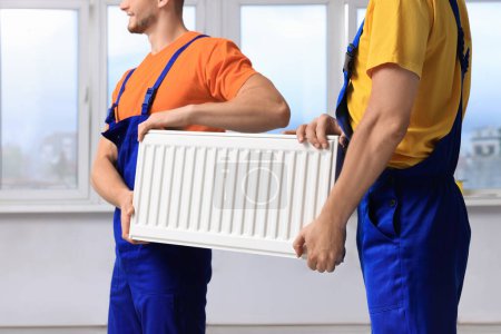 Professional plumbers with new heating radiator indoors, closeup