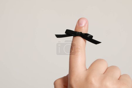 Photo for Man showing index finger with black tied bow as reminder on white background, closeup. Space for text - Royalty Free Image